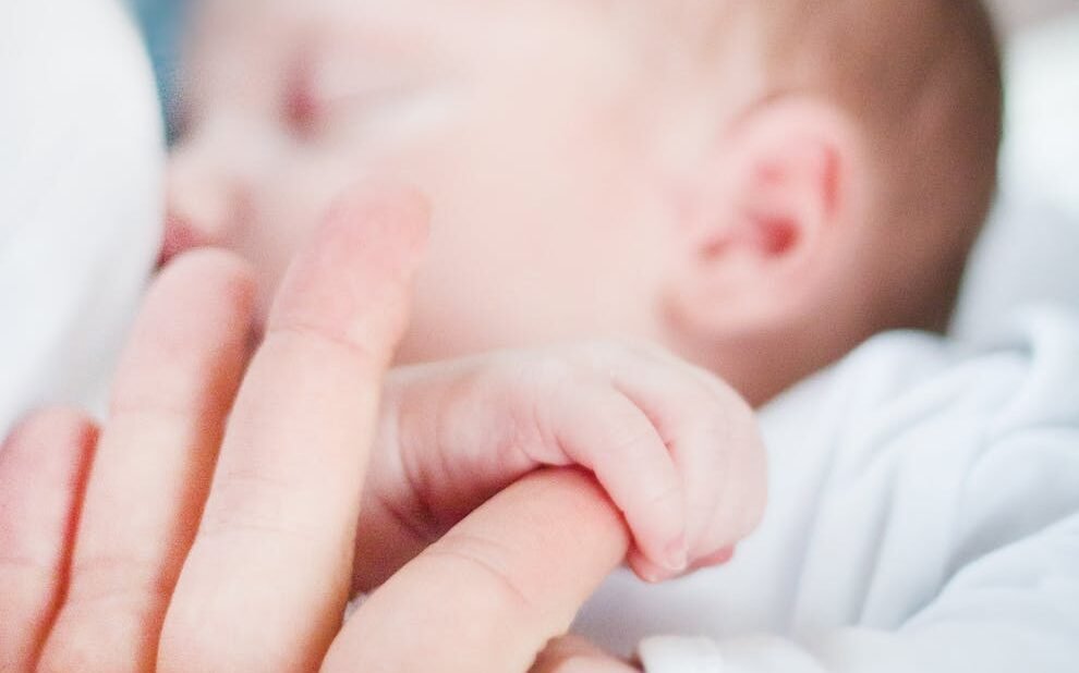 foto da mão do bebê segurando o dedo de um adulto durante a amamentação.